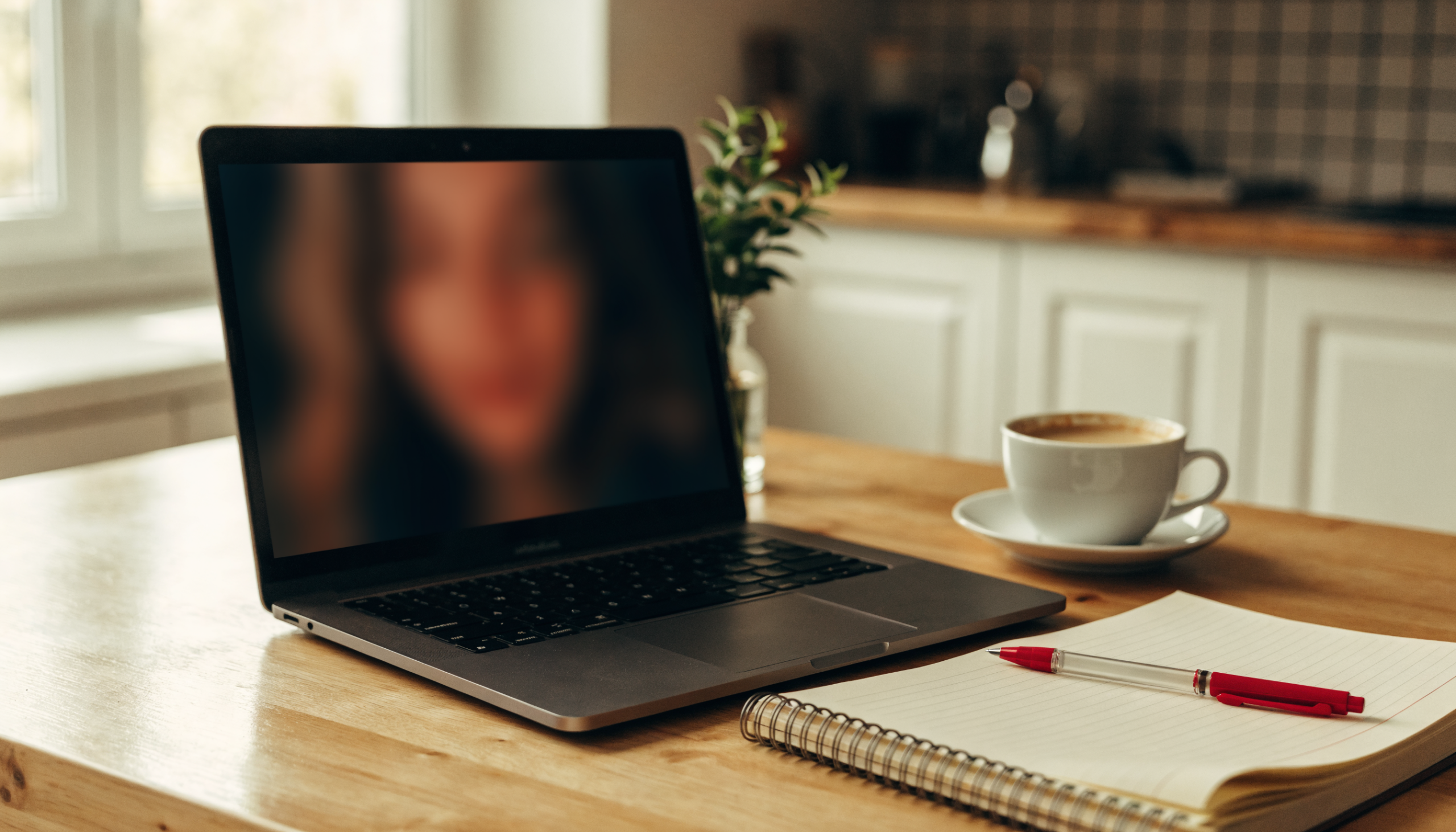 An open laptop playing a training lesson beside a notebook and coffee on a kitchen table